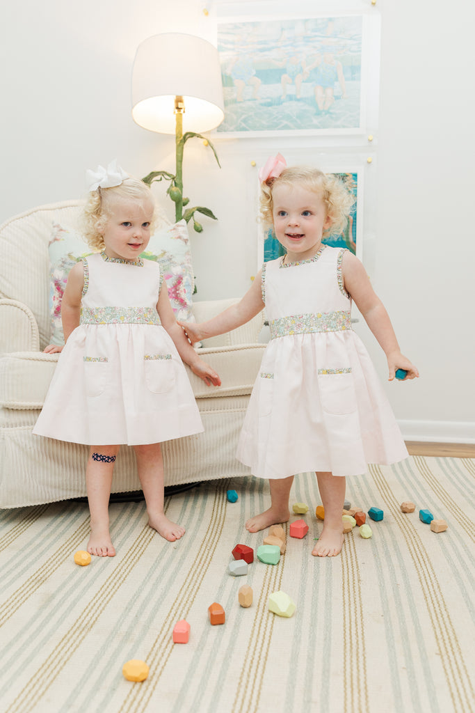 Two young girls in matching dresses standing on a carpet with colorful toys around them.